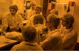 A group of people in the clean room with protective lab coats and hairnets.