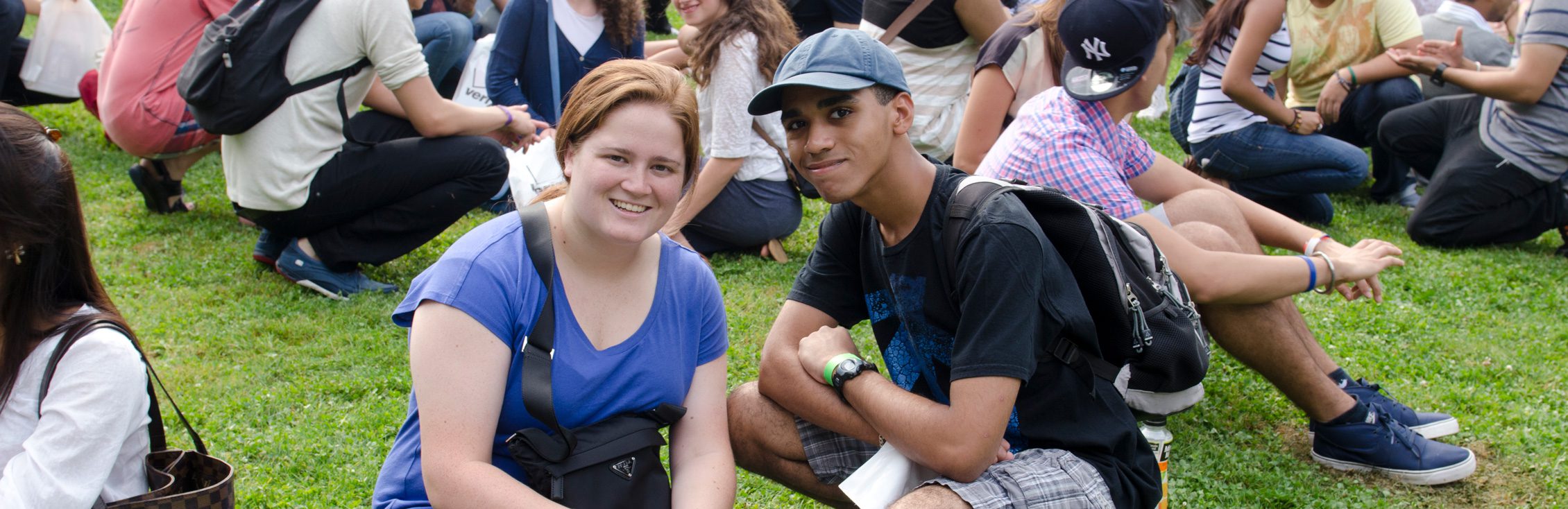 Two students looking at a laptop while sitting on the grass. 